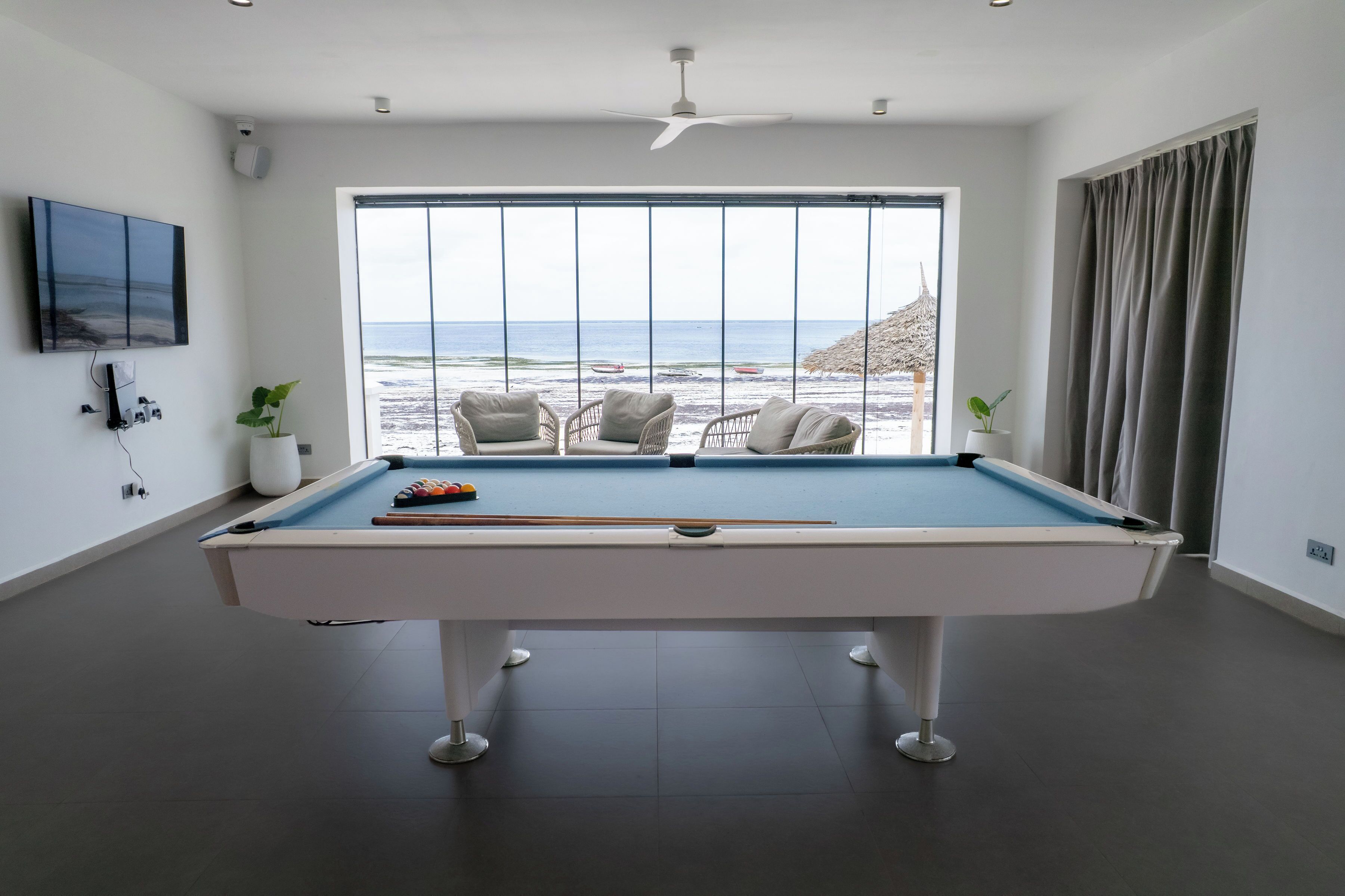 A pool table with a view of the beach, a ceiling fan, and a television on the wall.
