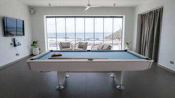 Una mesa de billar con vistas a la playa, un ventilador de techo y un televisor en la pared.