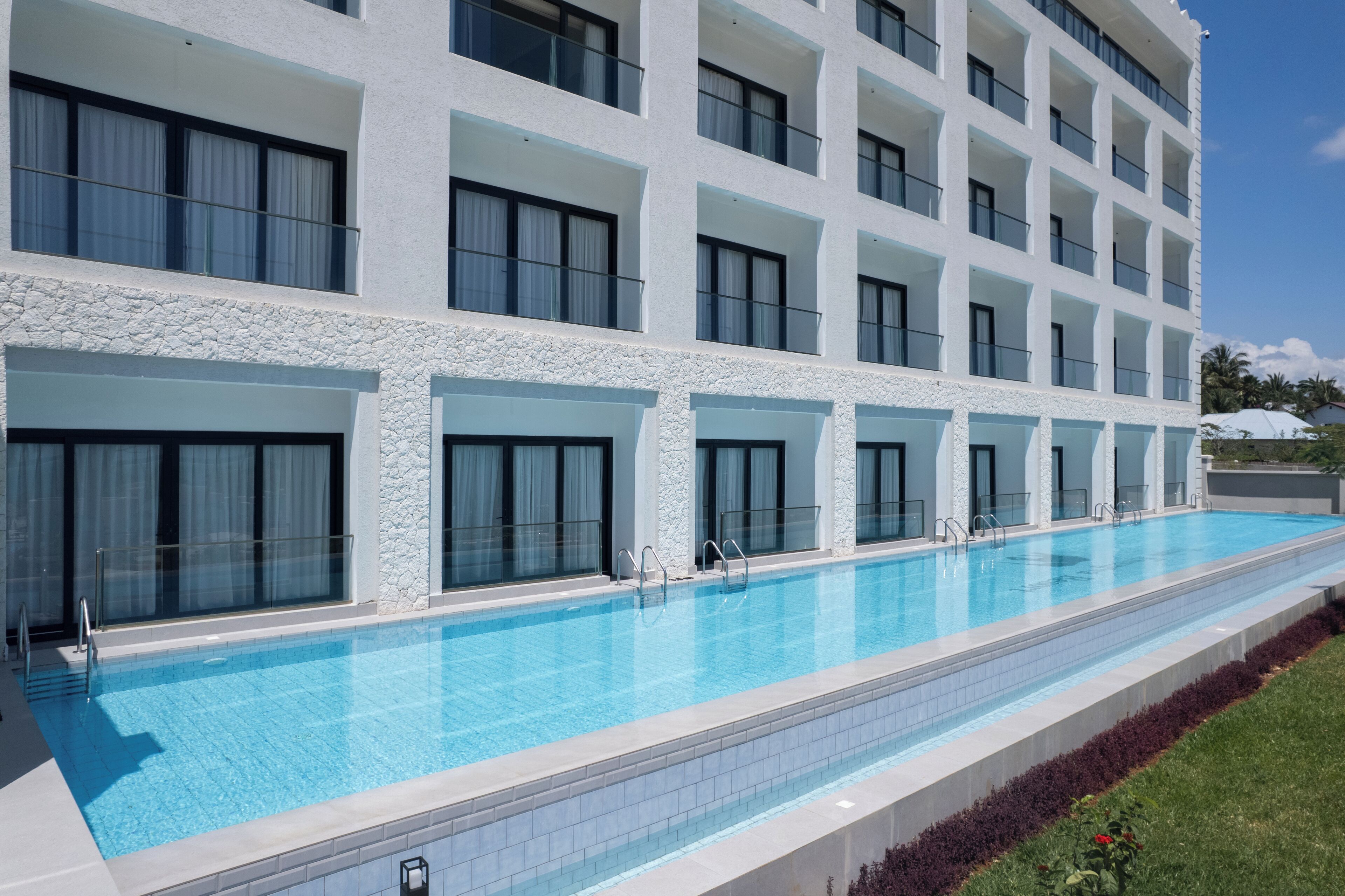Un hotel moderno con una piscina larga, varios balcones y fachada de piedra.