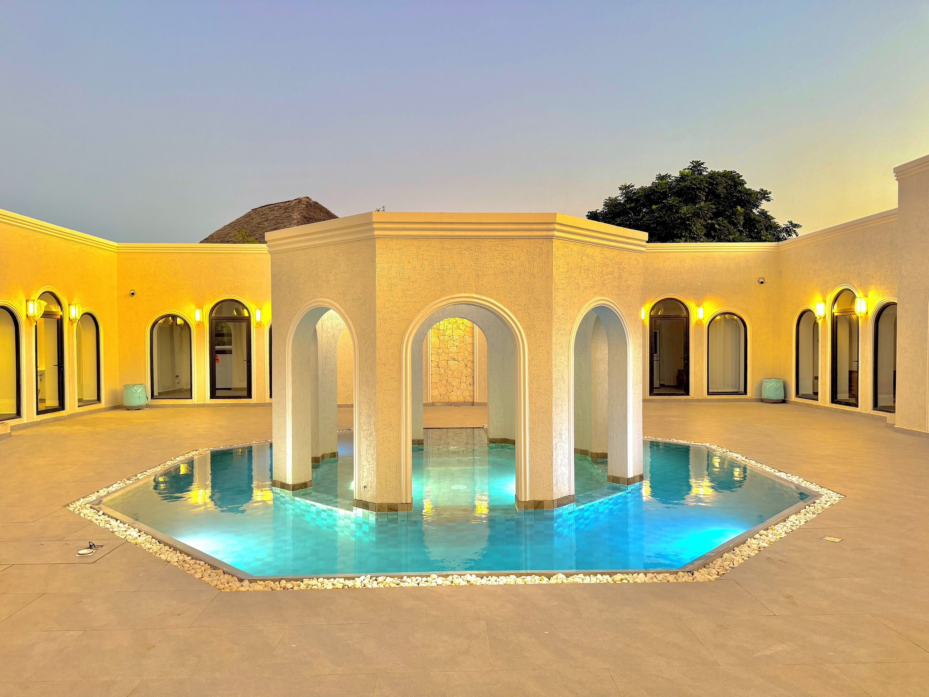 Zona de piscina amb una estructura central envoltada d'arcs, una piscina cristal·lina i un paviment de rajola.