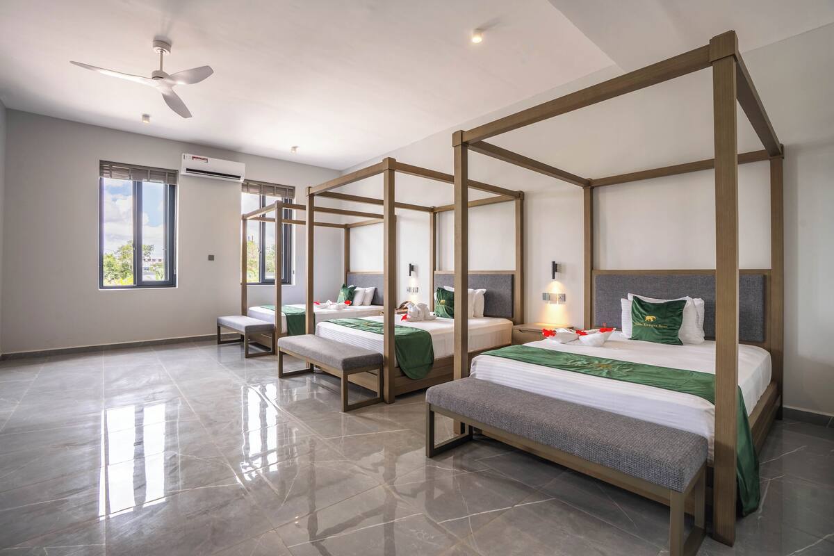 Een hotelkamer met vier hemelbedden, een plafondventilator, grote ramen en een betegelde vloer.