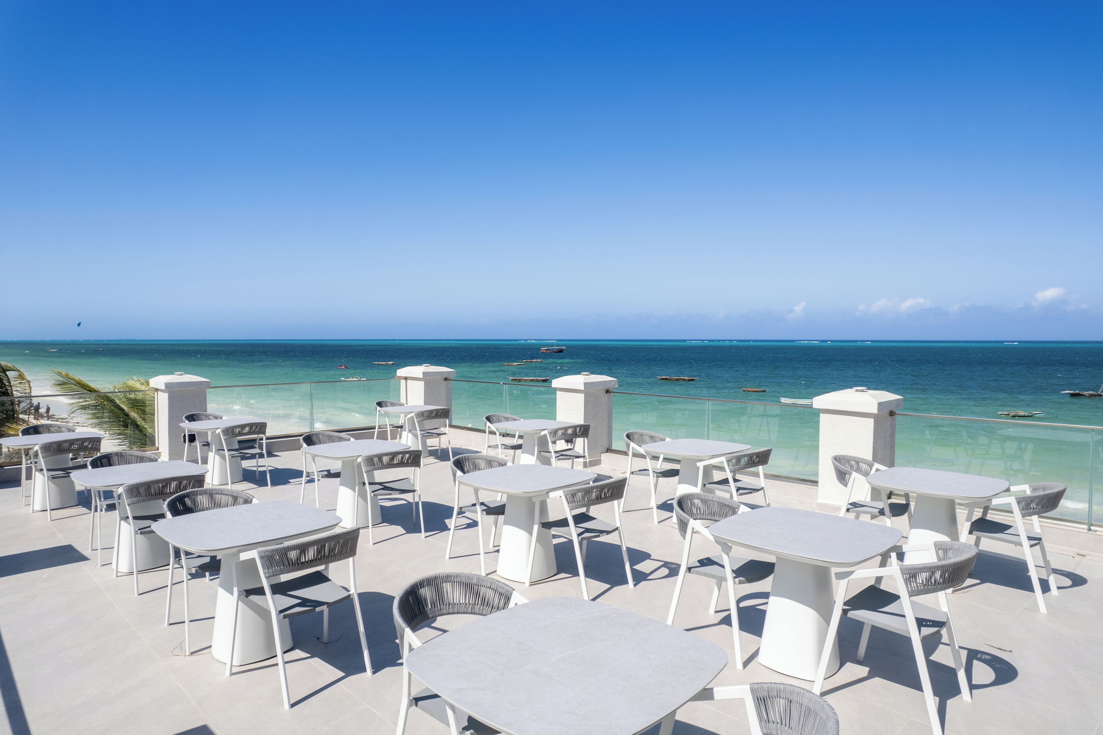 An outdoor seating area with tables and chairs overlooking a clear blue sea.