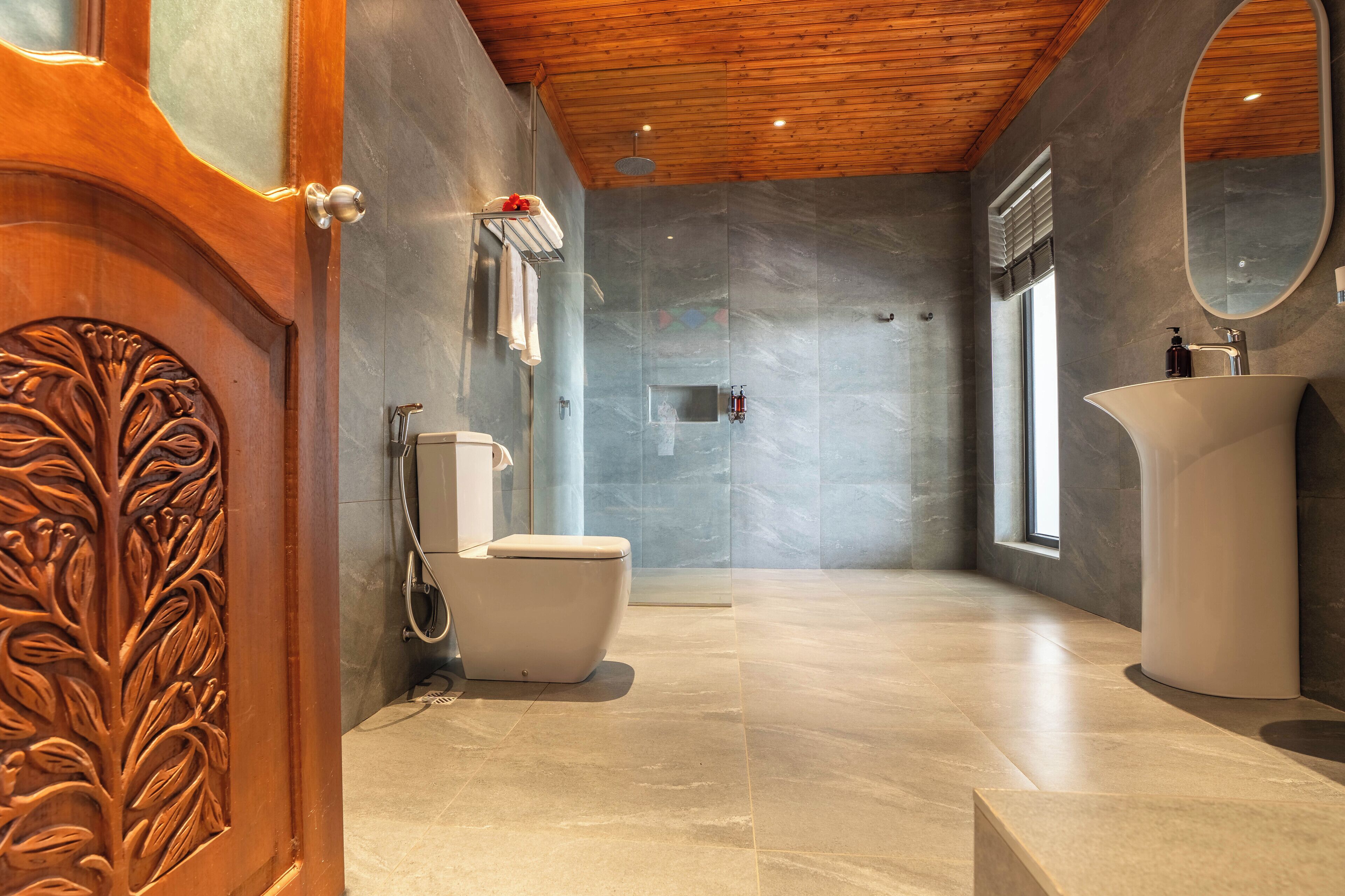 Une salle de bain moderne avec un plafond en bois, un grand miroir, un lavabo blanc et un espace douche.