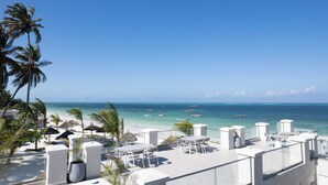 Terraza en la azotea con mobiliario blanco, palmeras y vista a la playa y al océano.