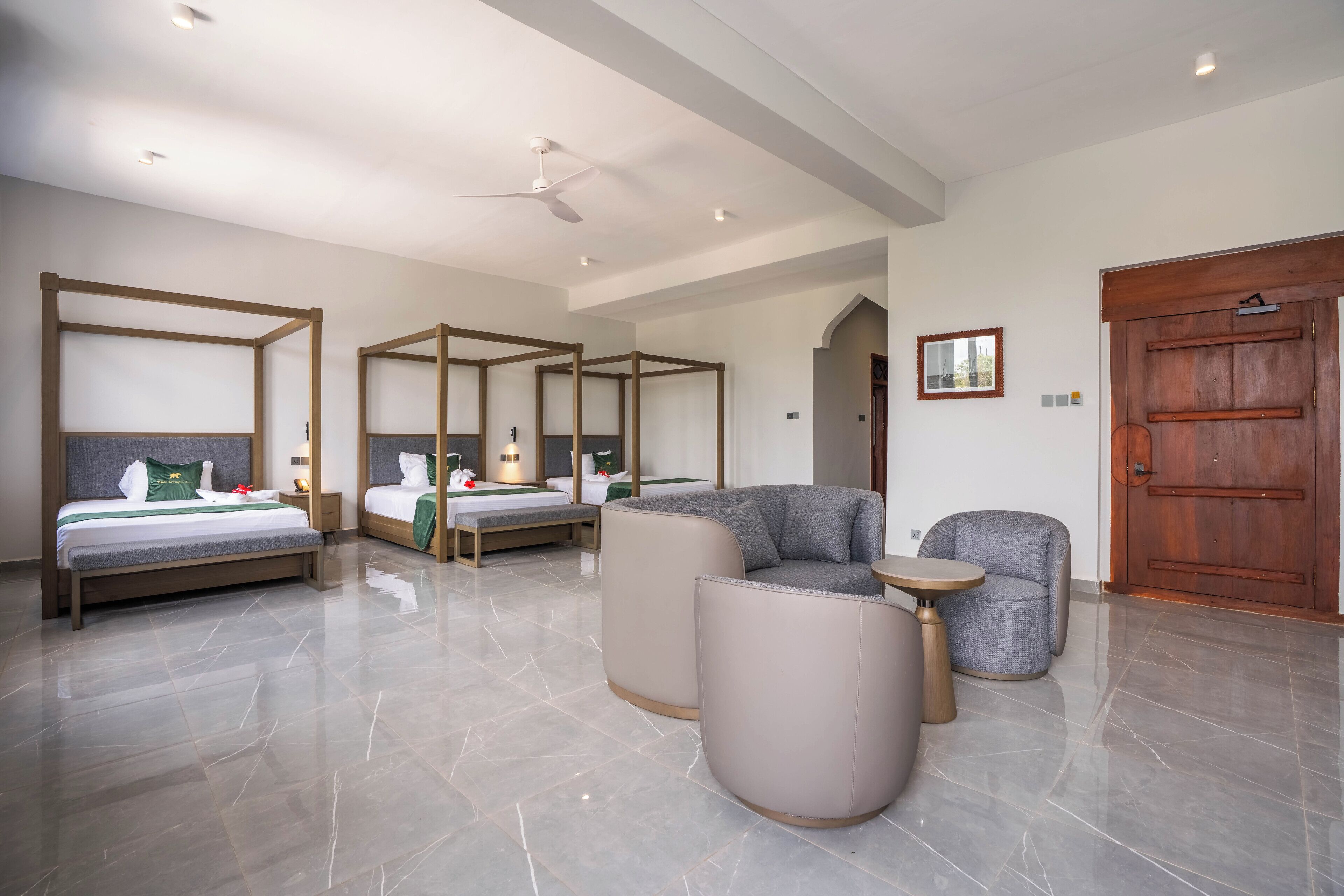 Une chambre d’hôtel moderne avec un grand lit, deux petits lits, un coin salon et une porte en bois.