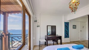 Un dormitorio con cama, escritorio, silla, ventana grande con vista al mar y candelabro.
