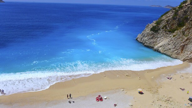 Una playa con agua azul cristalina, orilla de arena y acantilados rocosos.
