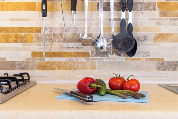 A kitchen counter with vegetables, a cutting board, and hanging kitchen utensils.