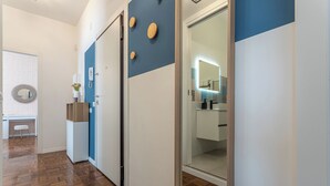 A hallway with a wooden floor, a blue and white wall, and a glass door leading to a bathroom.