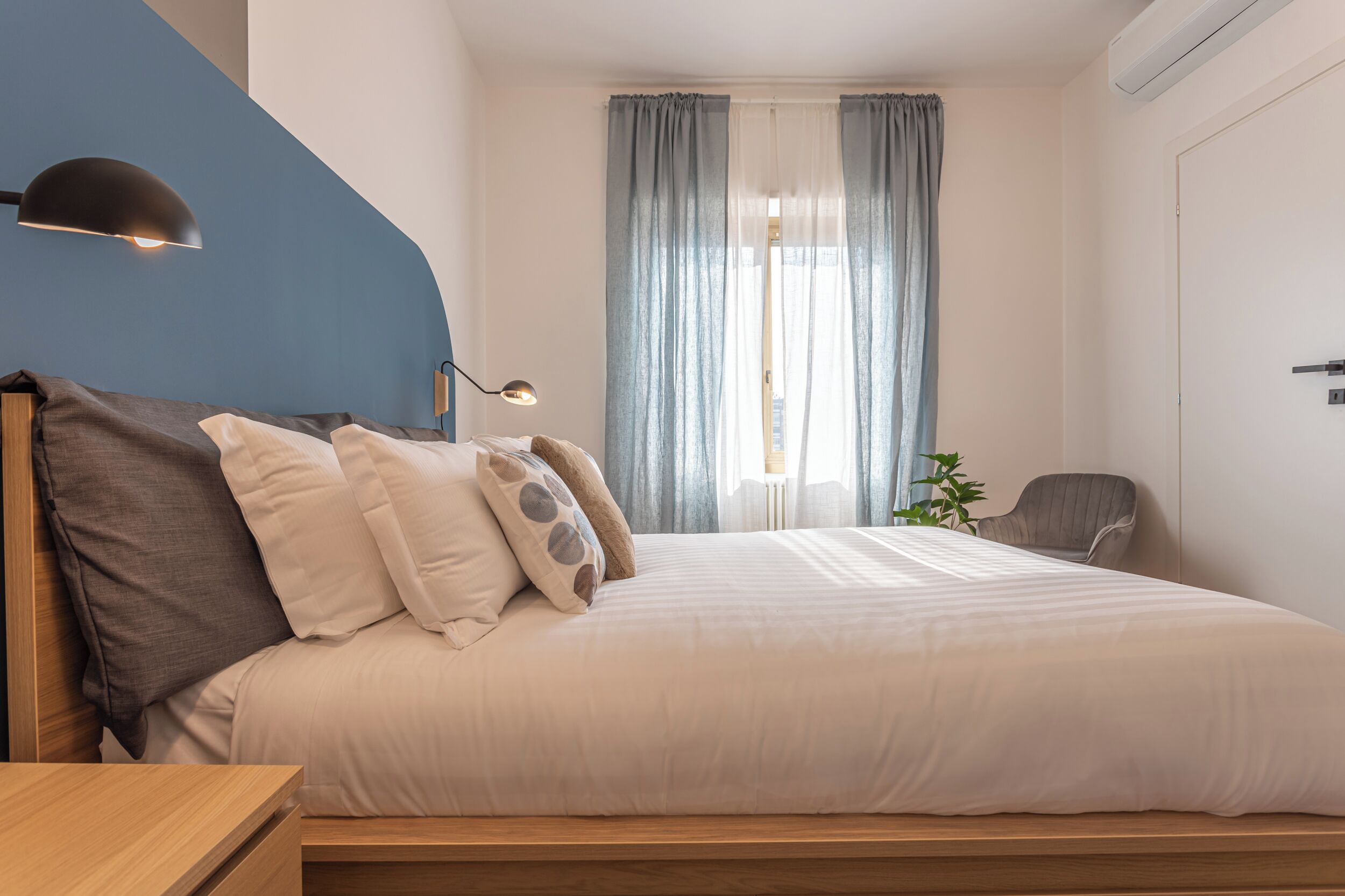 Quarto com cama, escrivaninha, cadeira, luminária e janela com cortinas.