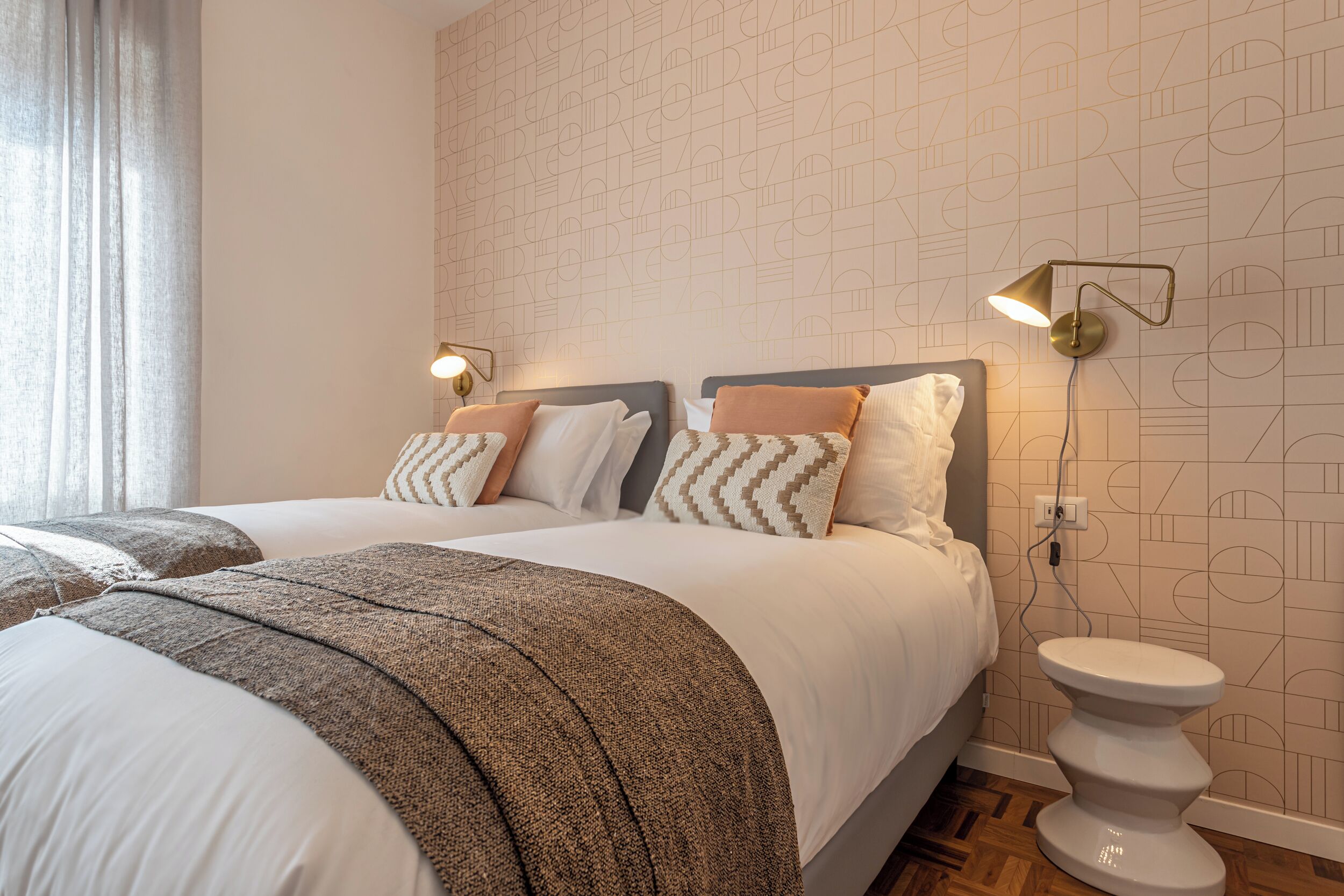 A hotel room with two beds, a modern wall design, and a bedside table with a lamp.