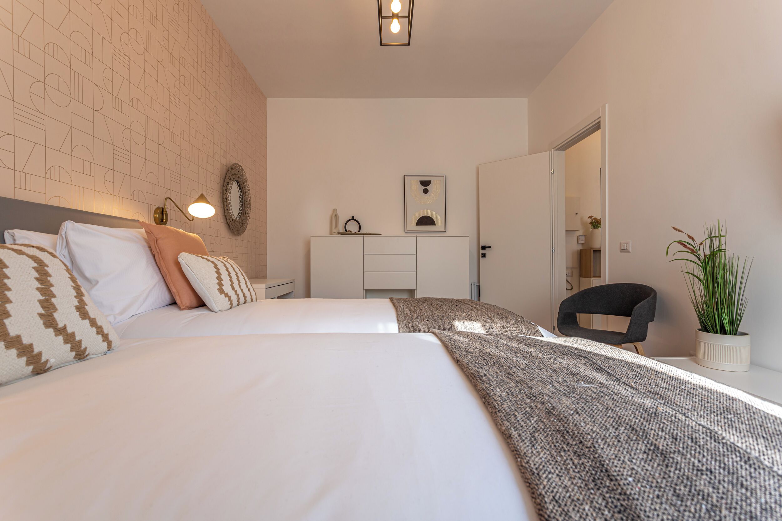 Un dormitorio moderno con dos camas, un escritorio, una silla y una planta en maceta.
