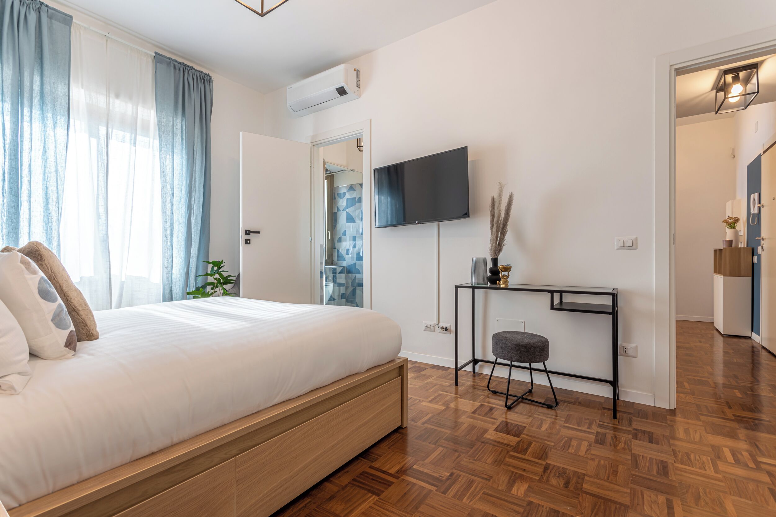Un dormitorio moderno con una cama de madera, un televisor montado en la pared y un pequeño escritorio con una silla.