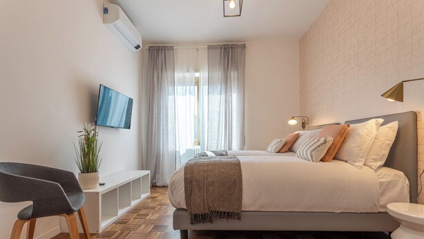 A modern bedroom with a bed, bedside table, TV, and a potted plant.