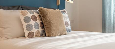 A neatly made bed with multiple pillows, a blue wall, and a wall-mounted lamp.