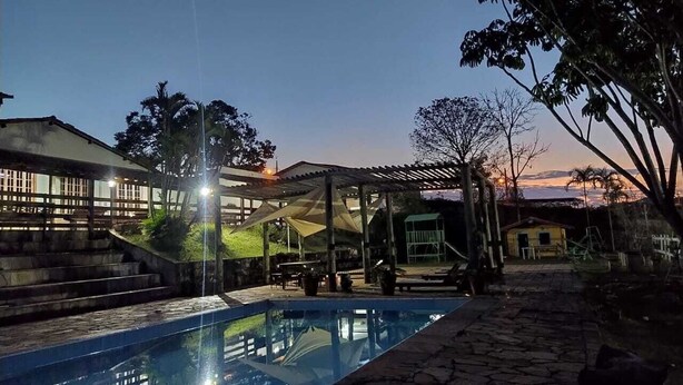 A swimming pool with a stone pathway, a covered seating area, and a building with a staircase in the background. - vereda bike park hotel (São João del Rei)