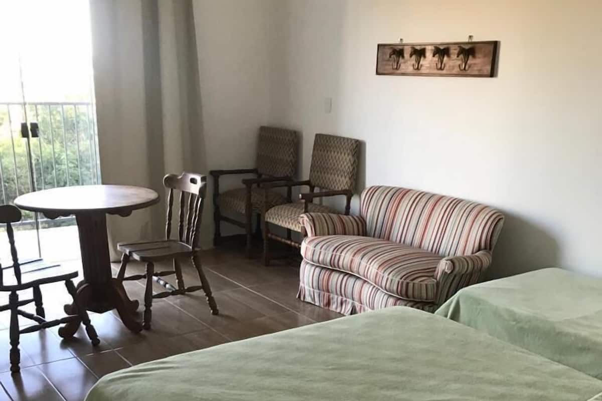 A hotel room with a bed, two chairs, a table, and a view of the outdoors.