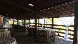 An outdoor patio with stone flooring, round tables with chairs, and a wooden ceiling structure. - vereda bike park hotel (São João del Rei)