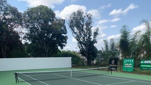 A tennis court with a net, surrounded by trees and a white wall. - vereda bike park hotel (São João del Rei)