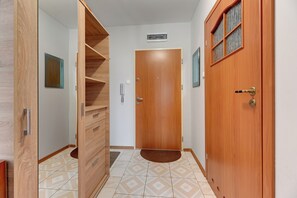 Un couloir avec une porte en bois, un miroir et un sol carrelé.
