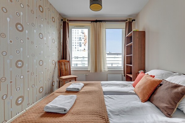 Une chambre d’hôtel avec un lit, une chaise, une armoire et une fenêtre donnant sur des immeubles.