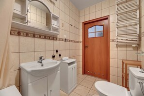 Une salle de bain avec deux lavabos, des toilettes, une douche et une porte avec une fenêtre.
