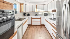 A modern kitchen with white cabinetry, wooden accents, a built-in oven, a microwave, a coffee maker, and a stainless steel refrigerator. - Retro Retreat Central Location Garage (Grand Junction)