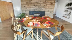 A round wooden table with six chairs, a stone wall behind, and a fireplace. - Retro Retreat Central Location Garage (Grand Junction)