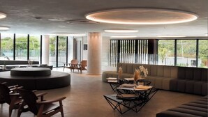 A modern lounge area with a circular seating arrangement, a central coffee table, and large windows offering a view of greenery. - Flat Porto Alto Resort, Porto de Galinhas   (N. São do Ó)
