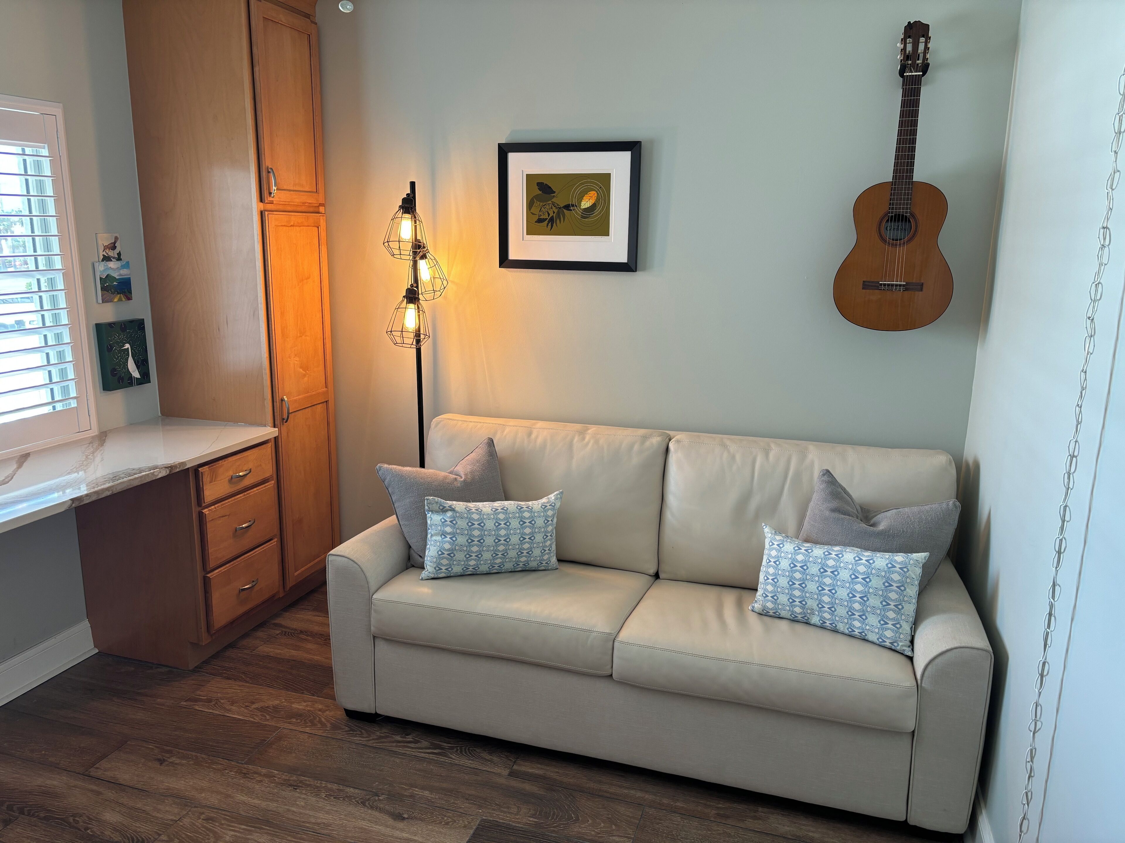 A cozy room with a beige sofa, a wooden cabinet, a framed picture, and a guitar on the wall.