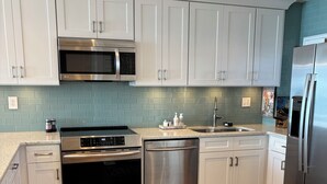 Una cocina moderna con gabinetes blancos, electrodomésticos de acero inoxidable y un salpicadero de azulejos azules.