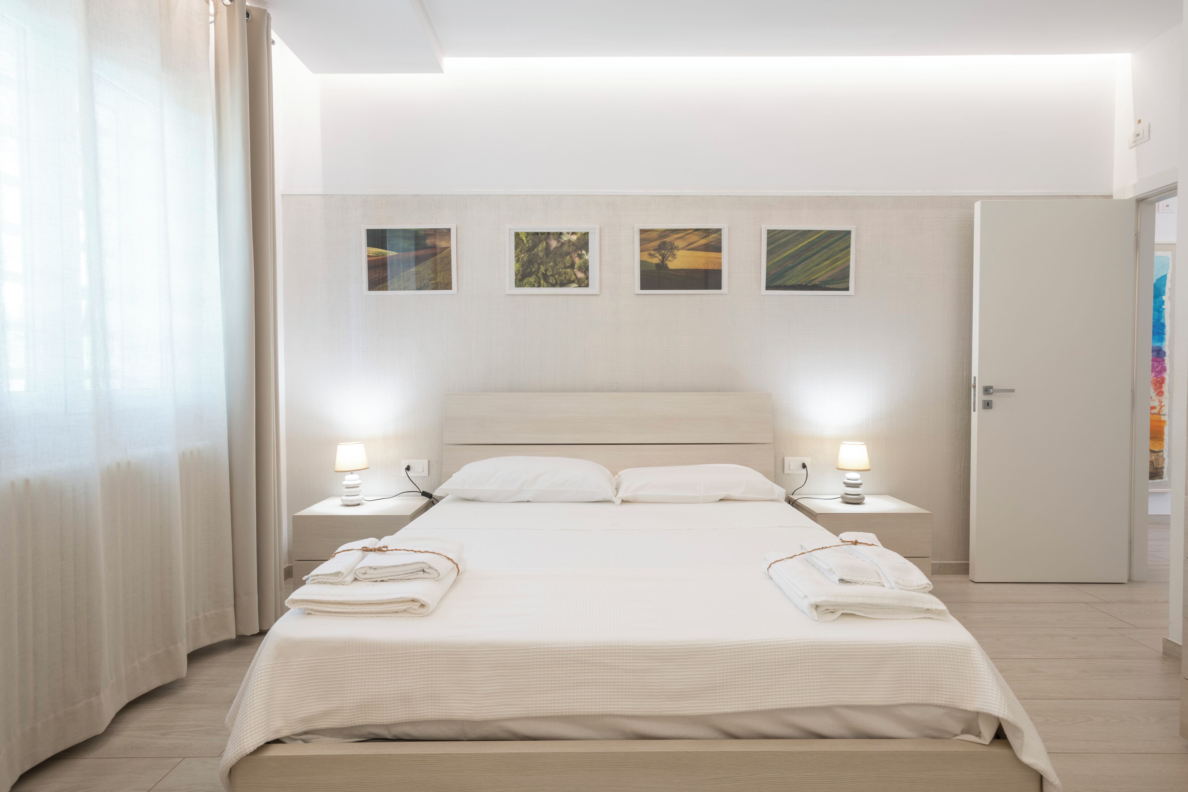 A modern hotel room with a large bed, two bedside tables with lamps, a wardrobe, and three framed pictures on the wall.