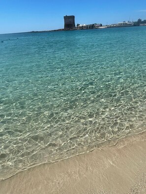 A beach with clear shallow water, a sandy shore, and a tower structure in the background.