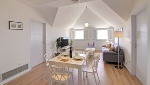 Ein modernes Wohnzimmer mit Essbereich, einem grauen Sofa und einem Fernseher auf einem Lowboard.