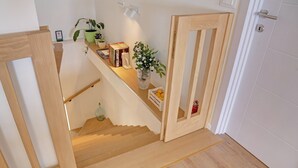 Eine Holztreppe mit einer weißen Wand und einer Tür auf der rechten Seite. Auf der Zwischenebene stehen Blumentöpfe, Bücher und eine kleine Vase.
