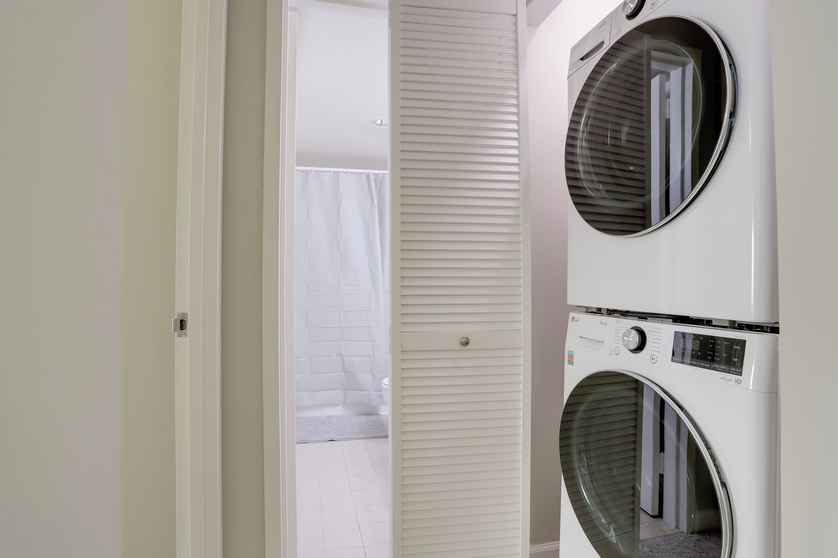 A laundry room with two stacked front-loading washing machines and a door leading to a bathroom with a shower and toilet.