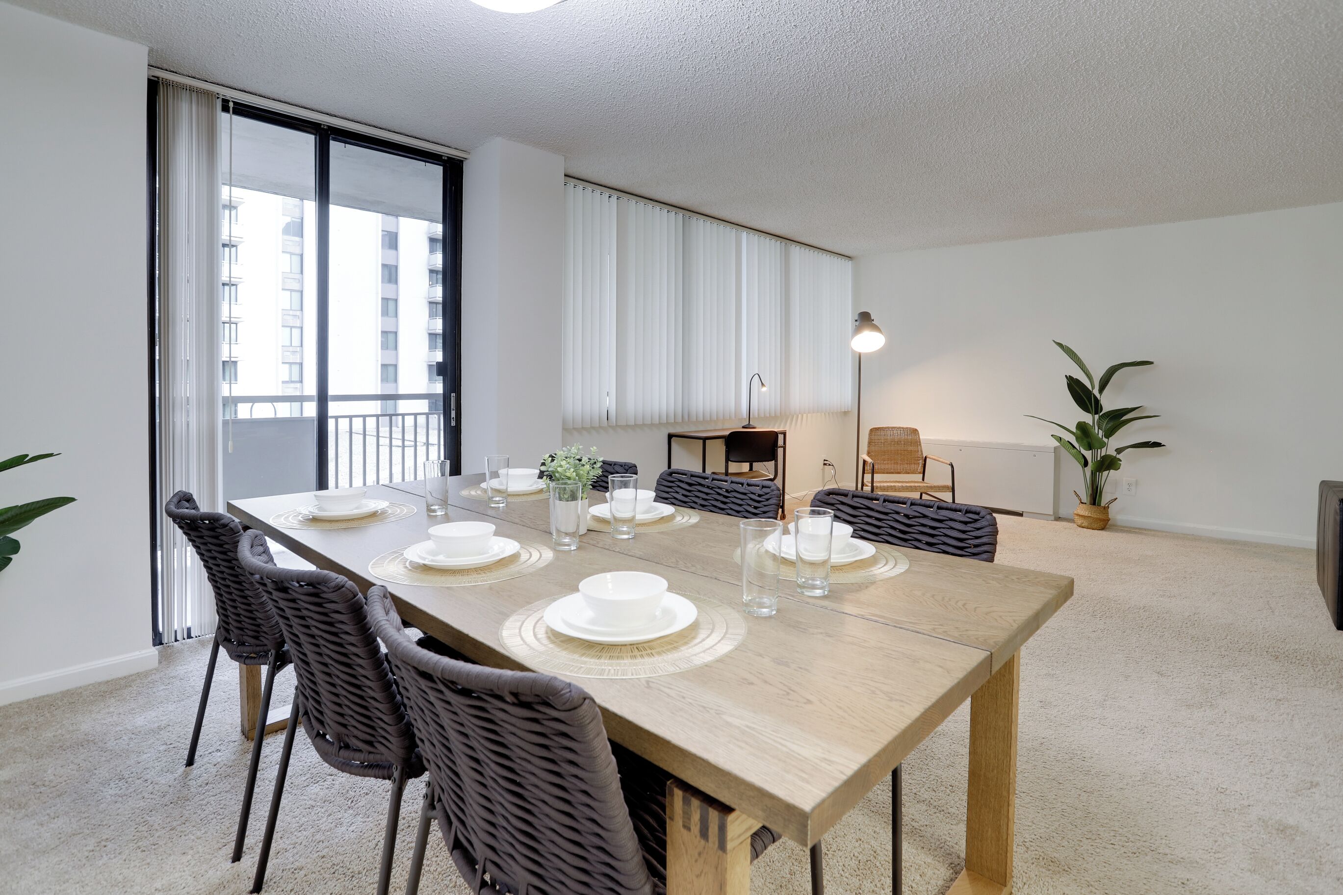 A dining area with a long wooden table set for four, surrounded by wicker chairs.