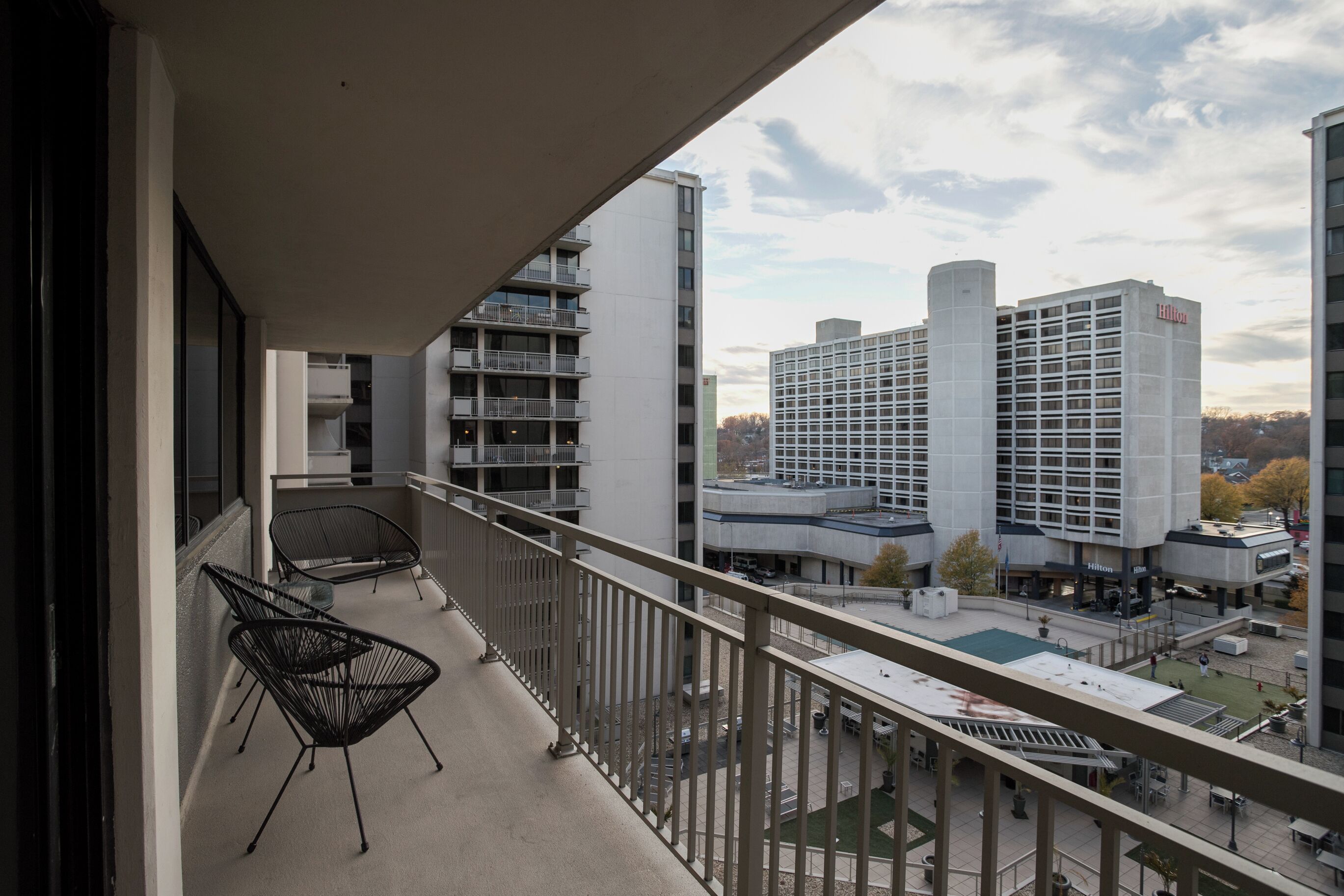Un balcon avec deux chaises noires, donnant sur un parking et sur le bâtiment d’un hôtel Hilton.