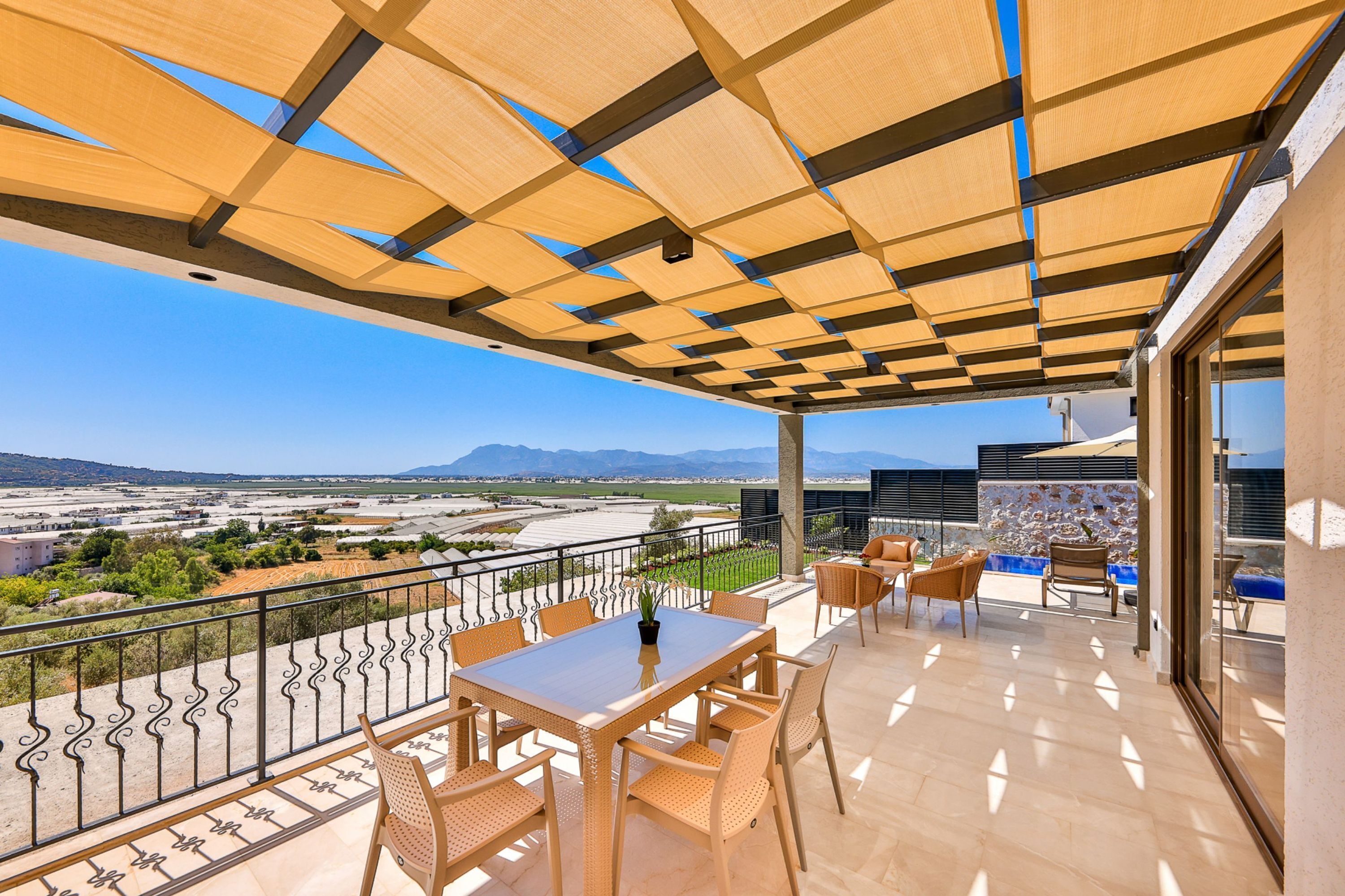 A terrace with a table and chairs, a view of a valley, and a mountain in the distance.