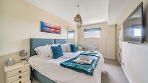 A bedroom with a large bed, a bedside table with a lamp, a TV, and a painting on the wall. - Cottage with 3 ensuite bedrooms and Sea Views.  North Devon Heritage Coast. (Bideford)