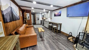 A modern living room with a brown leather sofa, a wooden coffee table, and a TV mounted on the wall. - Shamrock 73 - 2br/2ba - Pet Friendly - Fully Renovated! (Snowshoe)