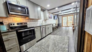 A modern kitchen with stainless steel appliances, grey cabinets, and a large window overlooking a deck. - Shamrock 73 - 2br/2ba - Pet Friendly - Fully Renovated! (Snowshoe)