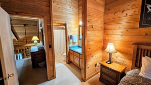 Ein Zimmer in einer Holzhütte mit Bett, Nachttisch und einem Badezimmer mit Duschvorhang.