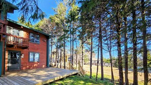 Eine Holzhütte mit einer Terrasse, umgeben von hohen Bäumen und blauem Himmel.