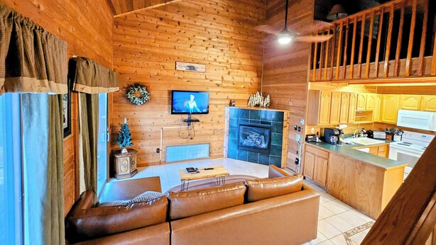 Ein gemütliches Blockhaus-Interieur mit Holzbalkendecke, Kamin, Fernseher und einer Küchenzeile.