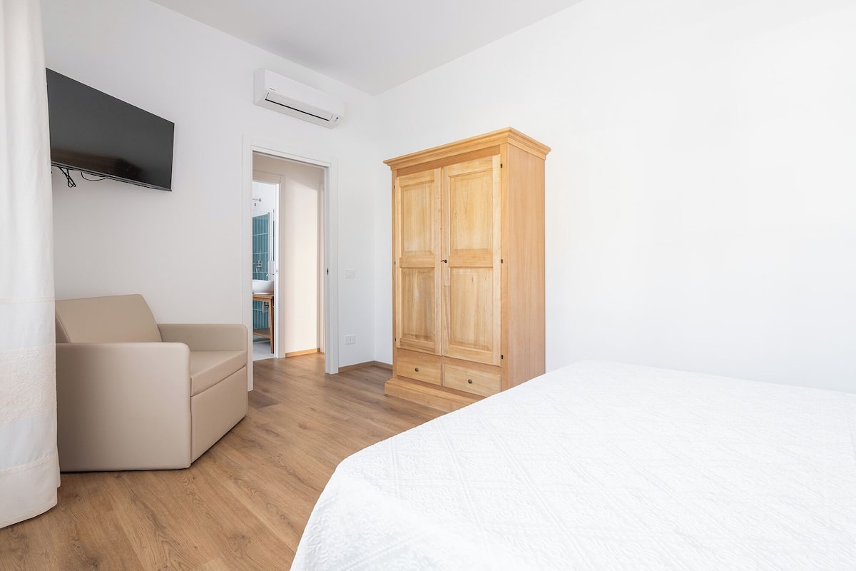 Un dormitorio con cama, un armario de madera, televisor montado en la pared y puerta que da al baño.