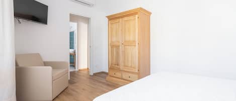 A bedroom with a bed, a wooden wardrobe, a TV mounted on the wall, and a door leading to a bathroom.
