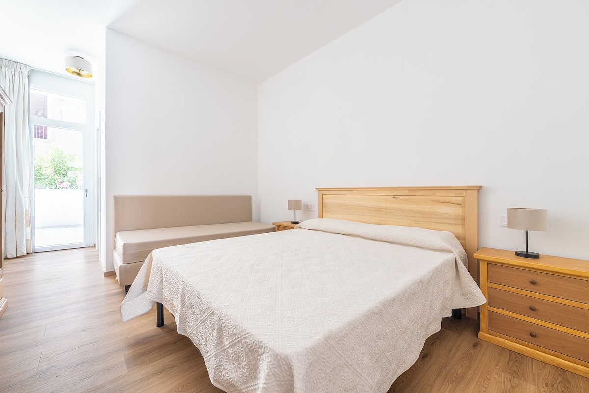 Un dormitorio con una cama de madera, dos mesitas de noche con lámparas, un banco y un aparador de madera.