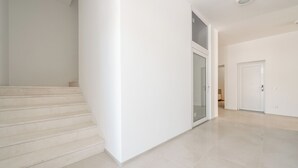 Interior limpio y moderno con una escalera que lleva a una puerta de cristal, una puerta blanca y un piso de baldosas.