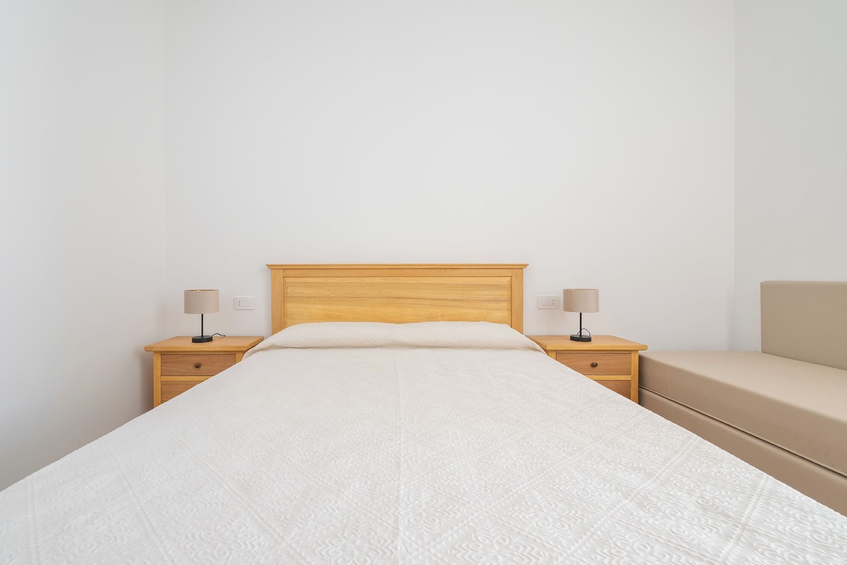 Un dormitorio con una cama de madera, dos mesitas de noche con lámparas y un sofá color beige.